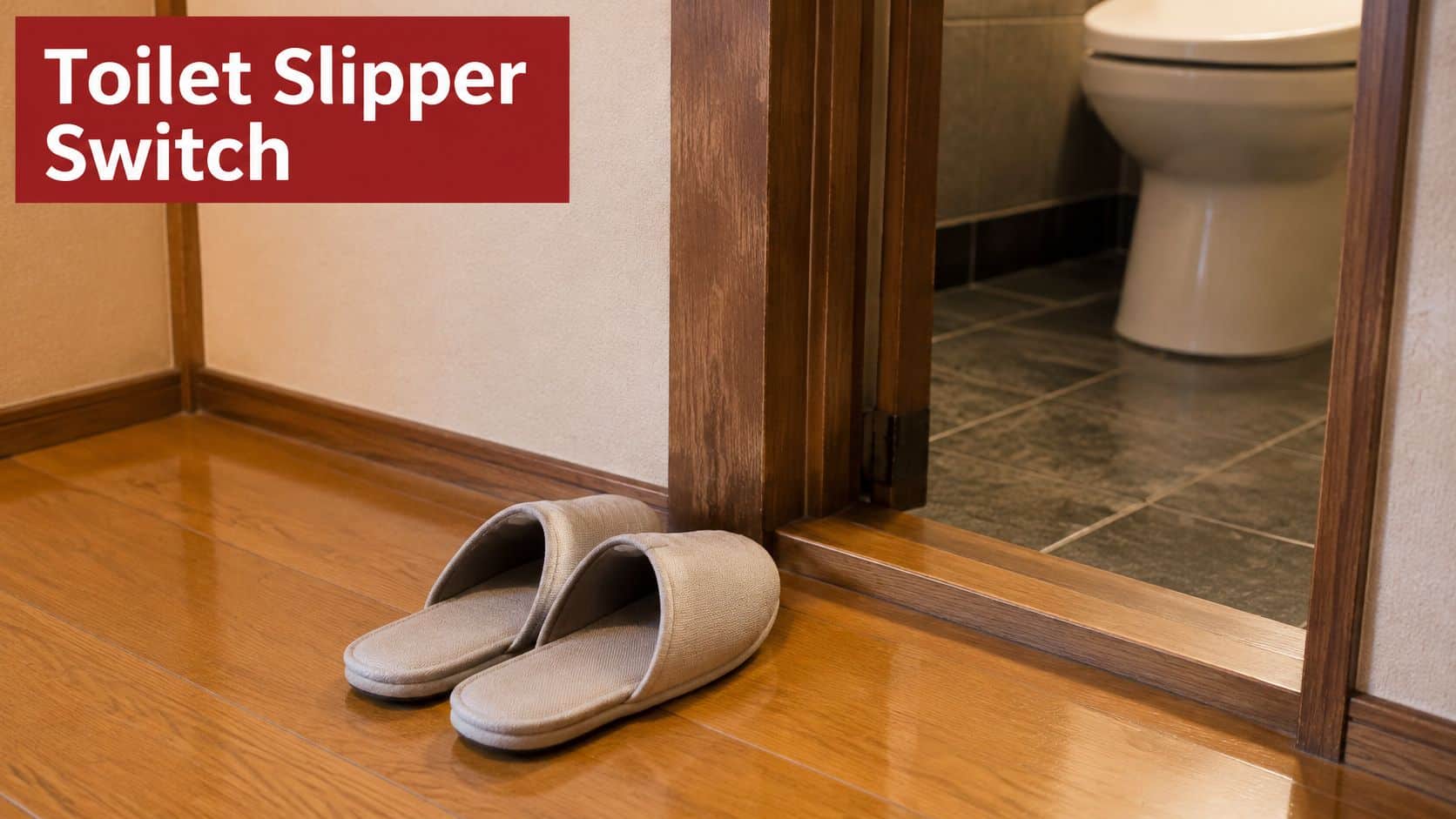 A pair of beige indoor slippers placed on a wooden floor near a bathroom entrance door.